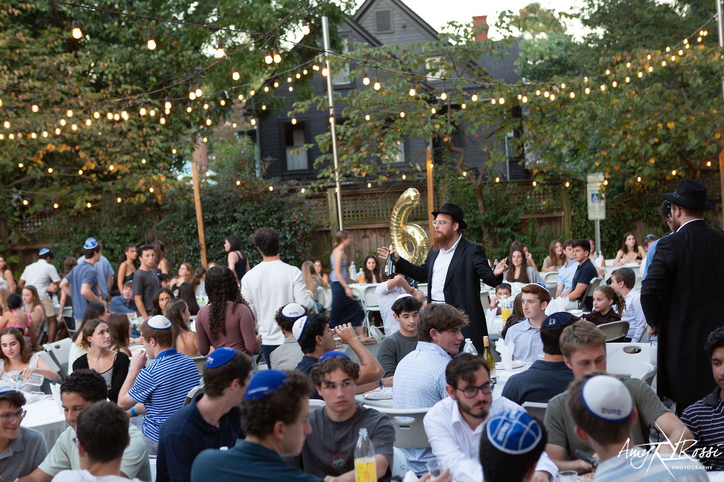 The backyard full of students under string lights, a birthday balloon floating above the tables
