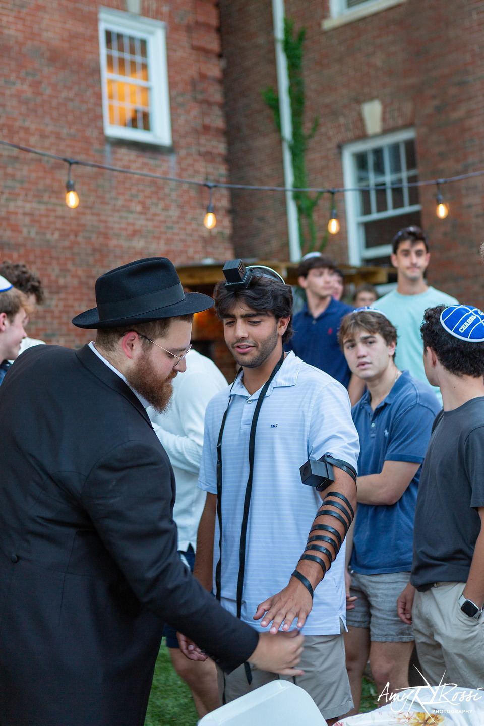 Rabbi Nossen wrapping tefillin with a student before dinner