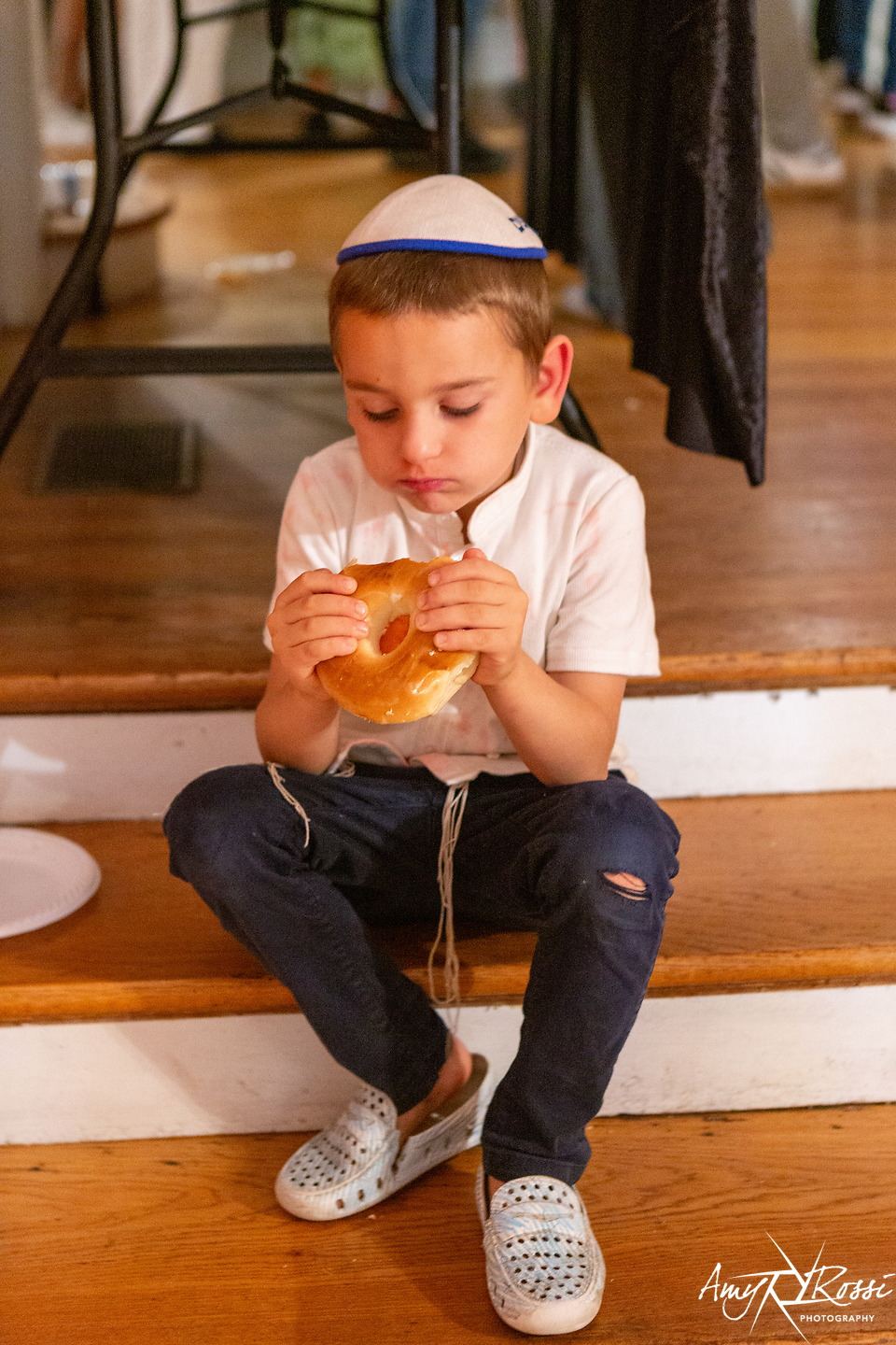 A boy in a kippah enjoying a bagel on the front steps